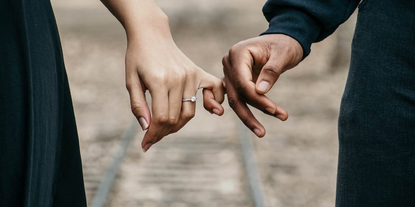 Two people standing with pinkie fingers interlocked.
