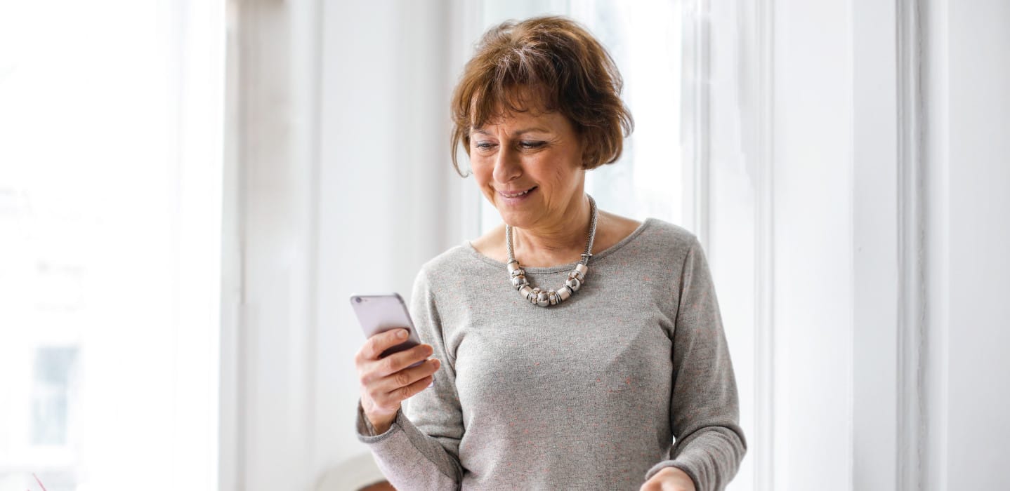 Woman wearing grey shirt looking at her phone.