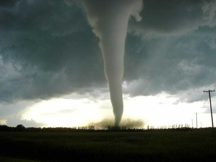 Tornado in field with trees on the horizon.