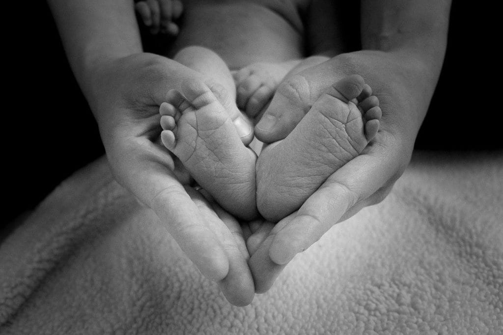Person holding hands in shape of a heart with baby feet in them.