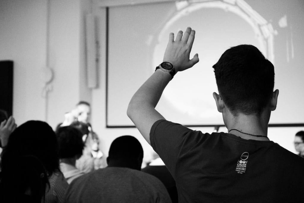 A man in the audience at an event raising his hand.