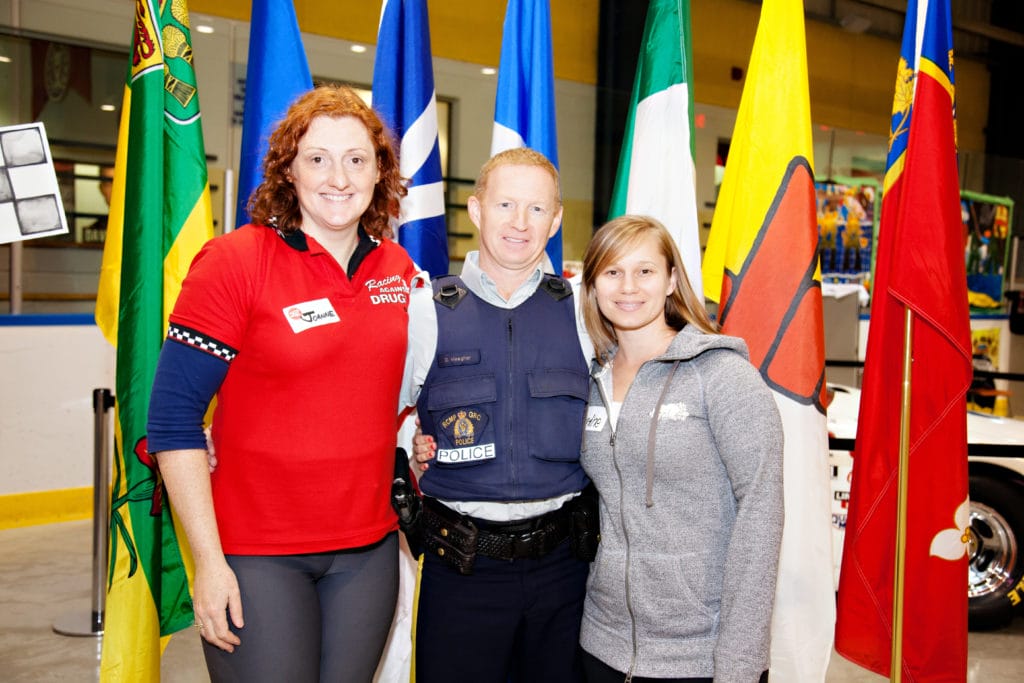 Two women standing next to a RCMP officer with different flags behind them.