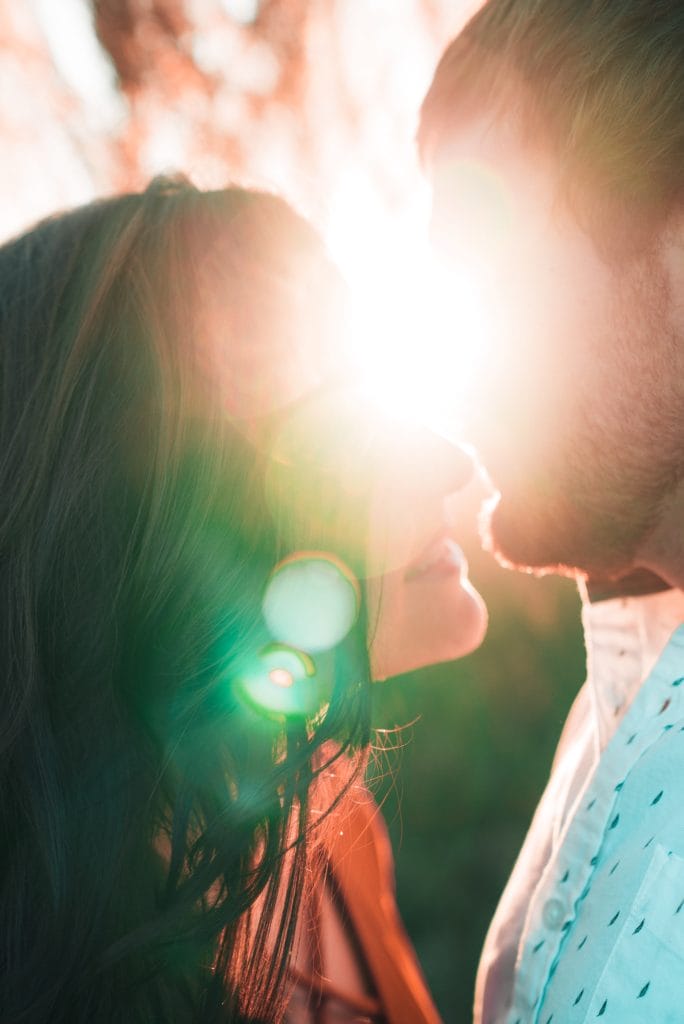 A couple facing each other about to kiss with a radiant sun light covering their faces partially.