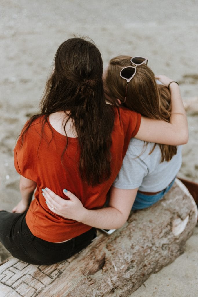 Two people embracing each other while sitting on a log at the beach.