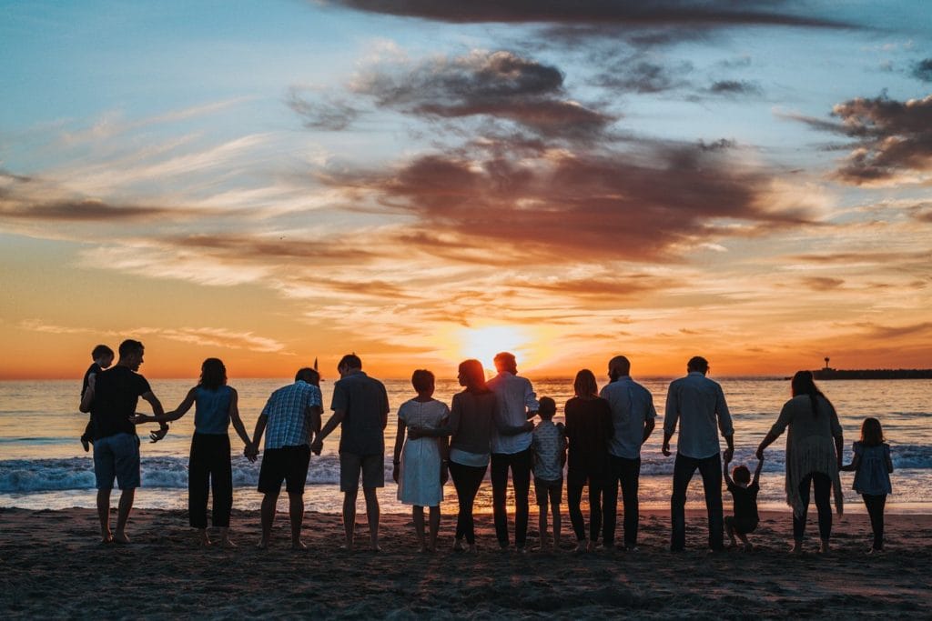 Group of people standing on the beach watching a sunset.