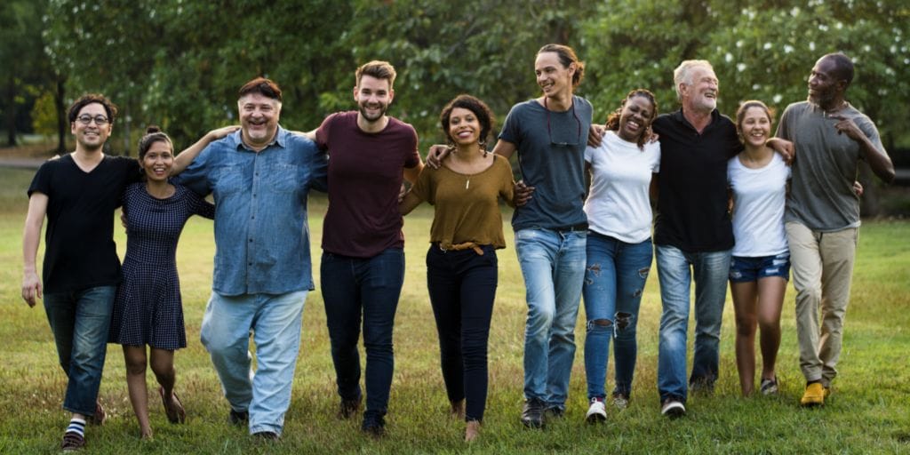 Diverse group of people walking arm in arm on grass.