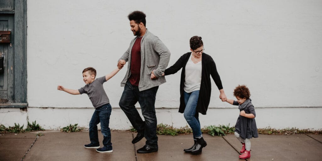 Family of four holding hands and walking down the sidewalk.