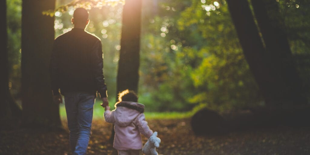 Father and child walking hand in handing the forest.