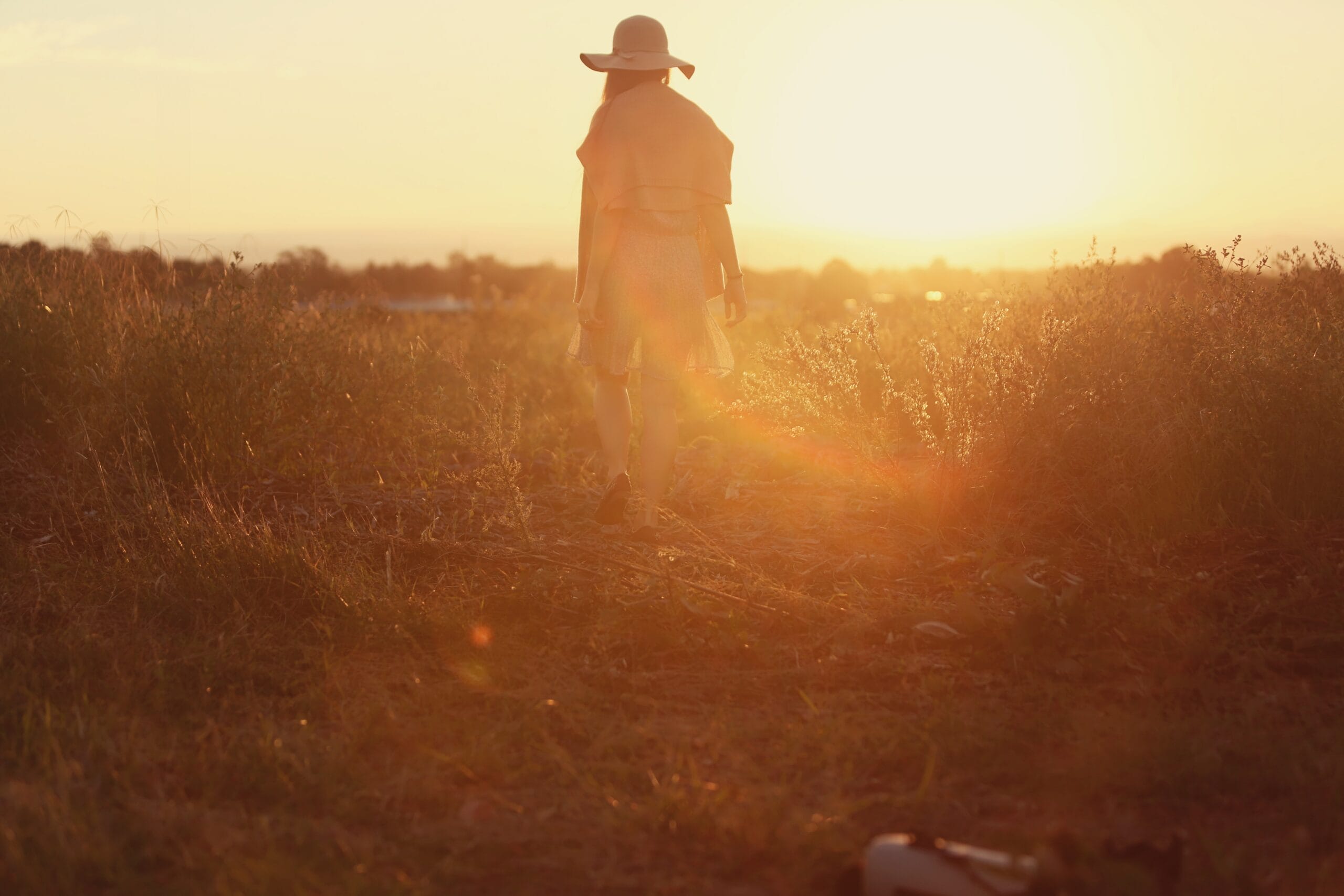 Person walking in field towards sunset.