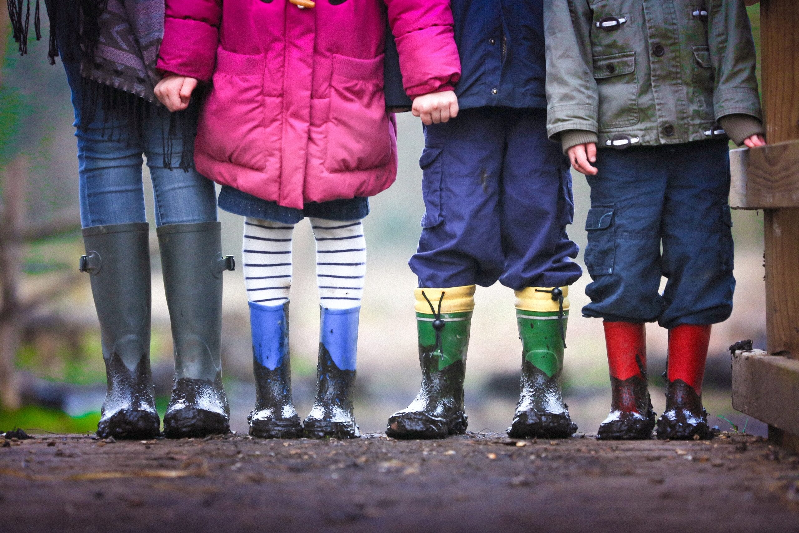 Four people standing in muddy rubber boots.