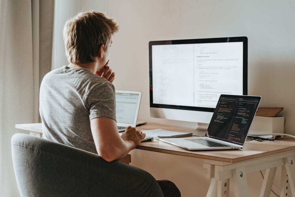 Person sitting at desk with three computers.