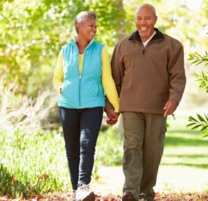 Couple walking on tree lined path holding hands and smiling.
