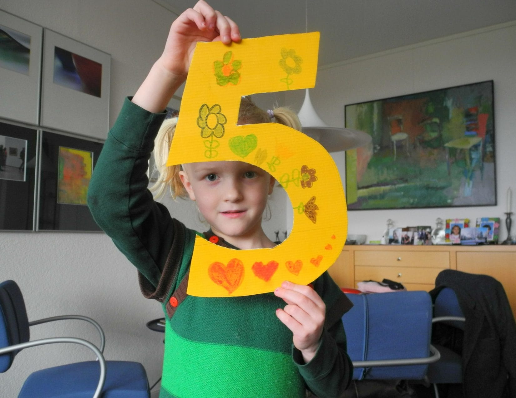 Child holding up a yellow number 5 with drawing on it