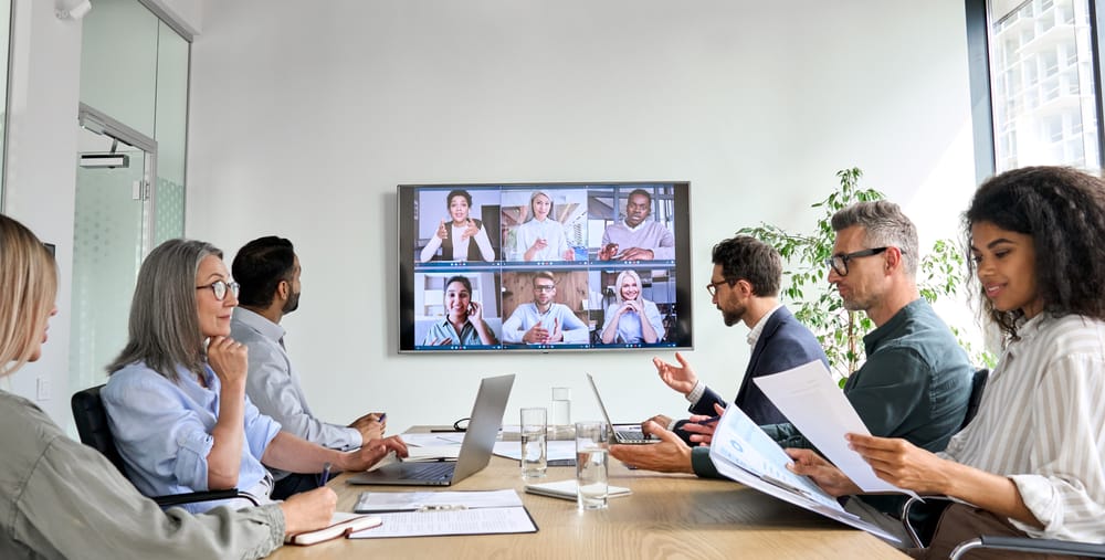 Group of people in boardroom having meeting with a group of people on a video call