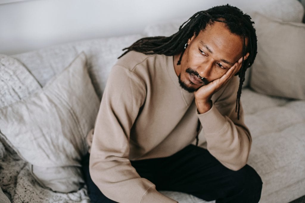 Man sitting on couch with head resting on hand.